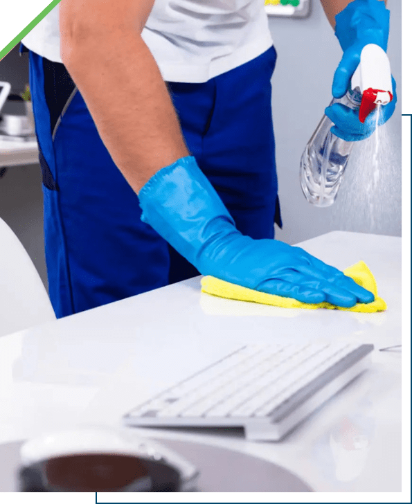 Person cleaning a desk with gloves and spray bottle.