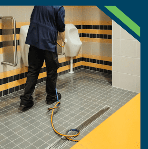 Person cleaning tiled floor with a pressure washer.